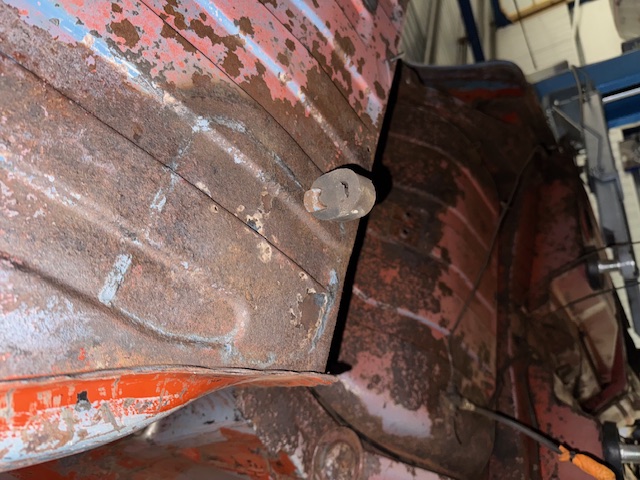 Underside of the KKH 295N body shell stripped to bare metal, showing red primer remnants, surface rust and a protruding bolt in a workshop